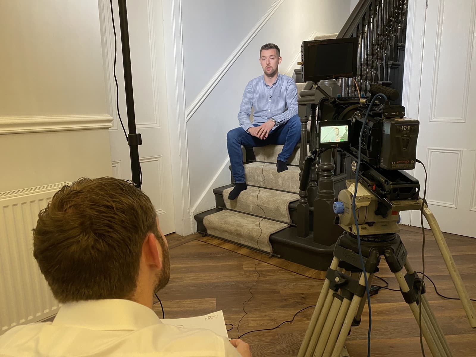 An agent interviewed on the stairs of a home, filmed on a tripod-mounted camera