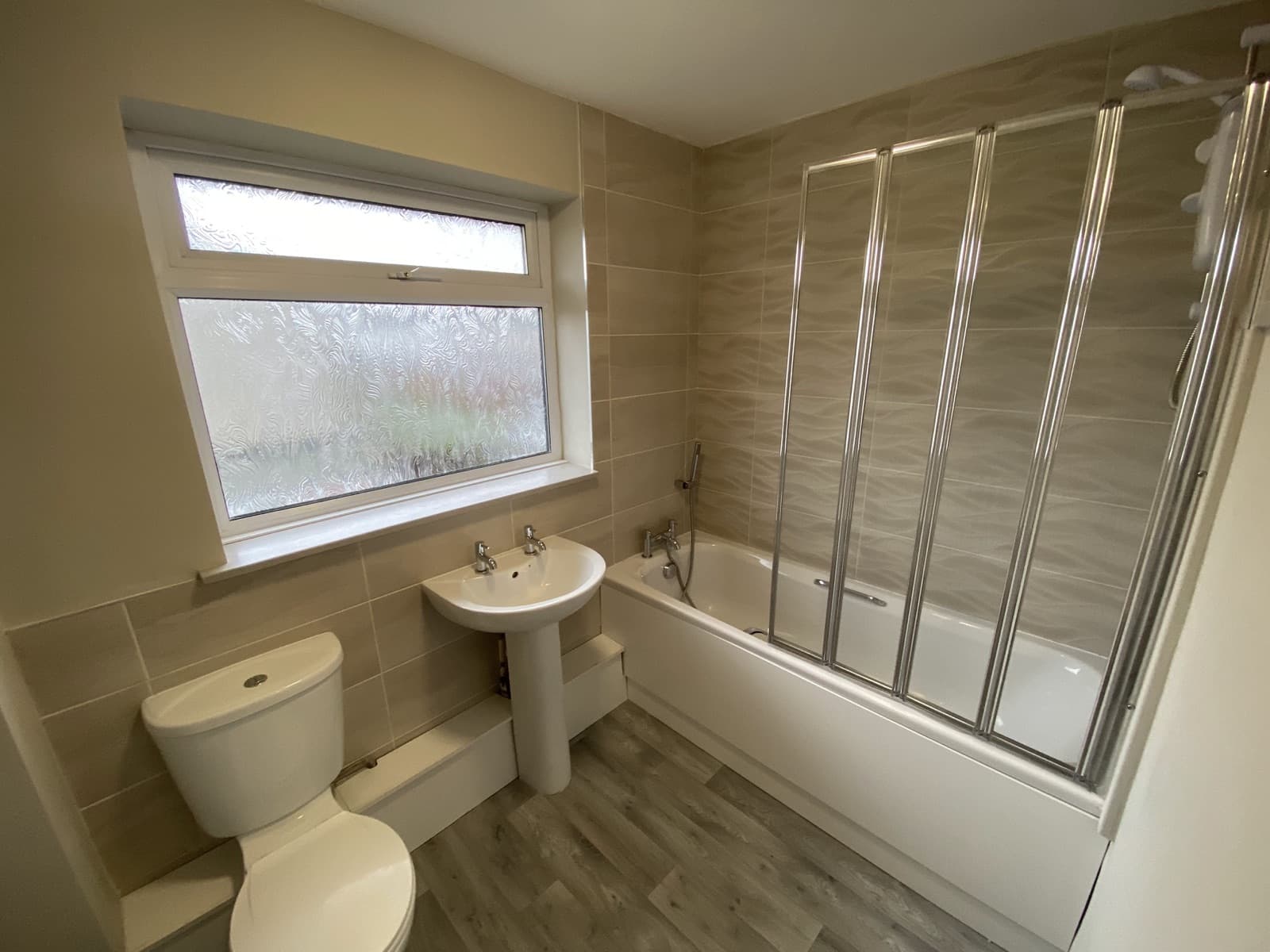 A tiled bathroom with a white suite and a bath screen