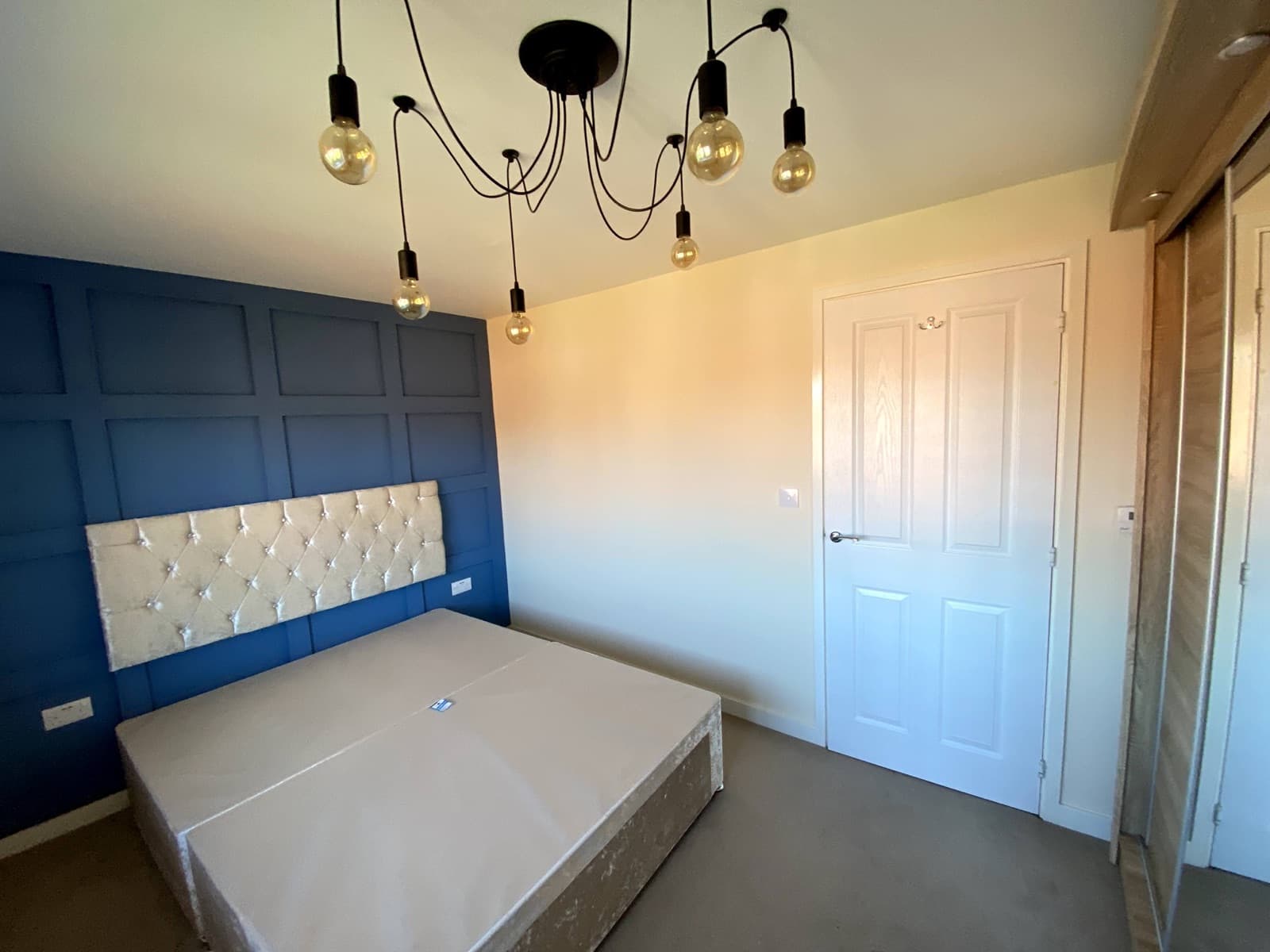 A double bedroom with a blue panelled feature wall and pendant lights