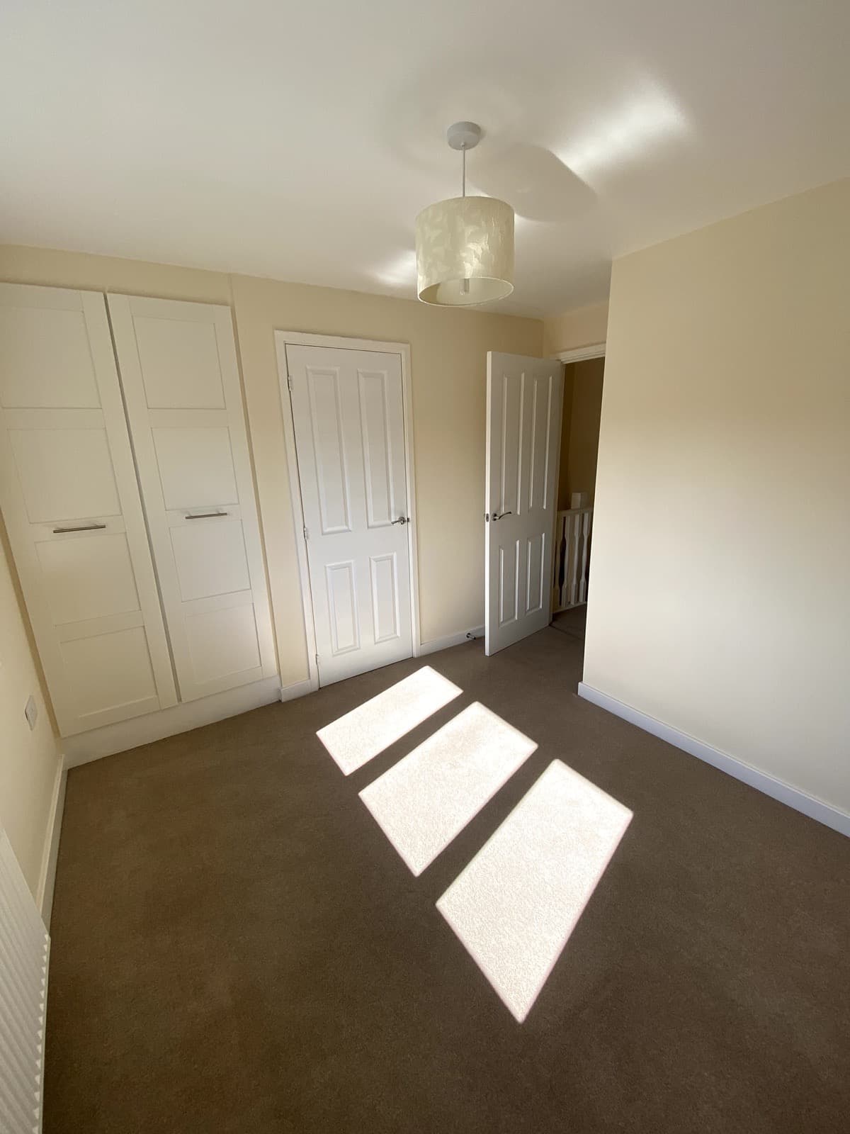 An empty double bedroom with fitted wardrobes and sunlight across the carpet