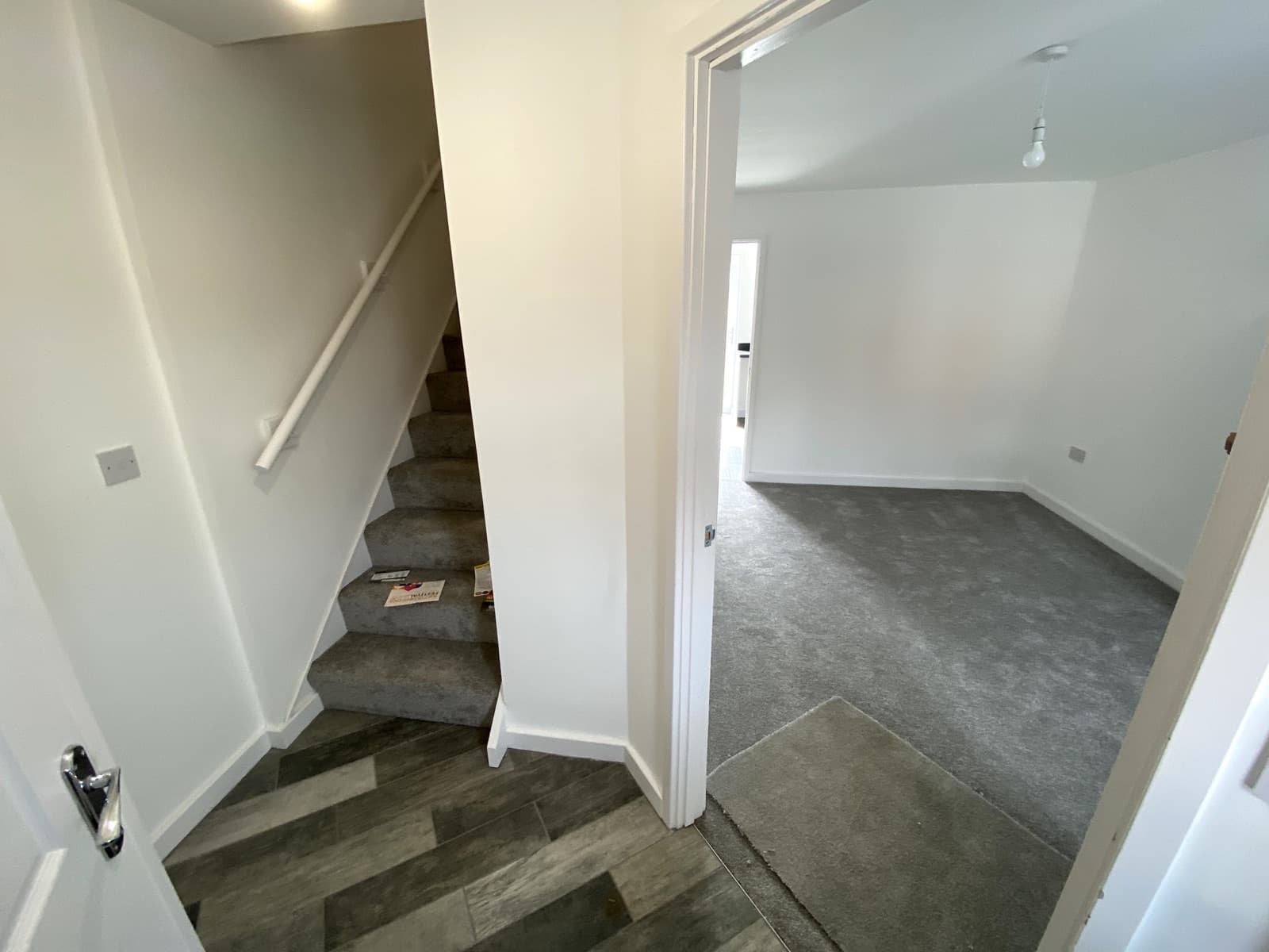 A hallway with a carpeted staircase leading off a bright front room