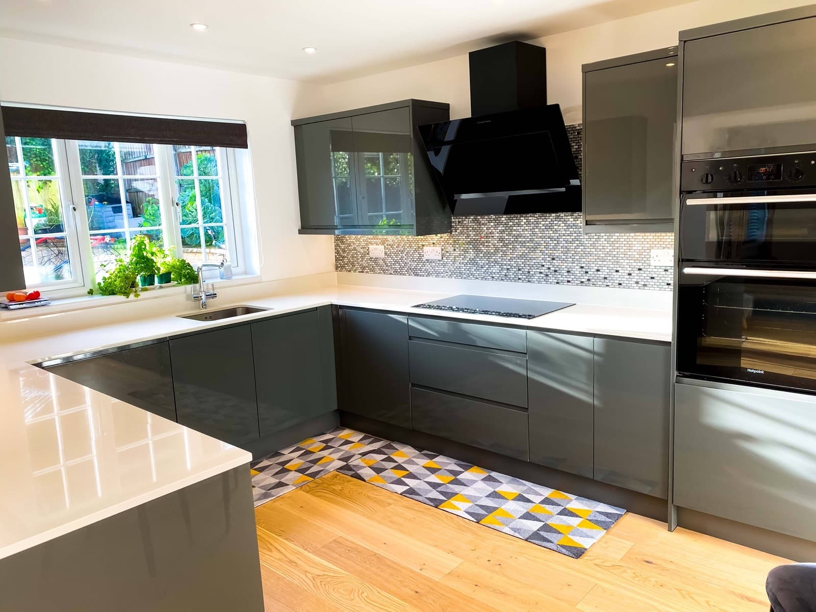 A grey gloss kitchen with white worktops and a garden view
