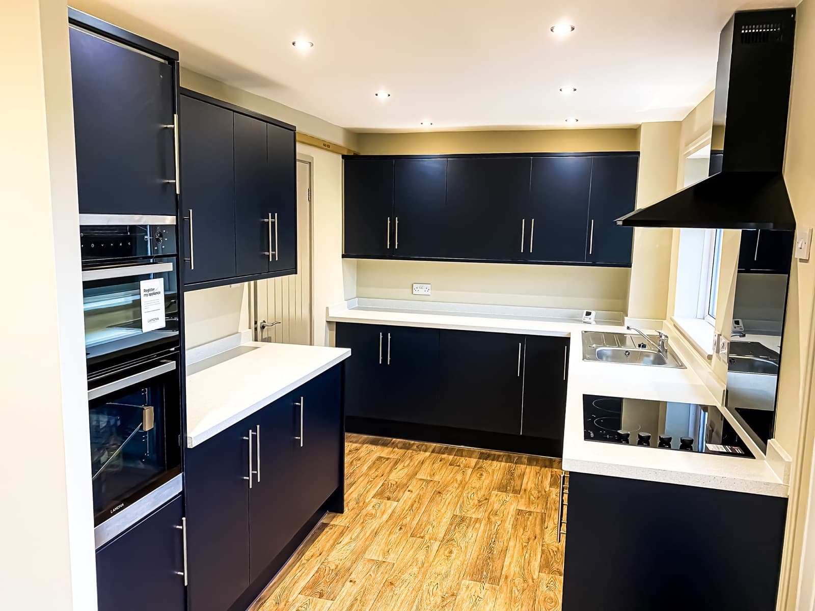 A newly fitted navy kitchen with built-in ovens and wood-effect floor