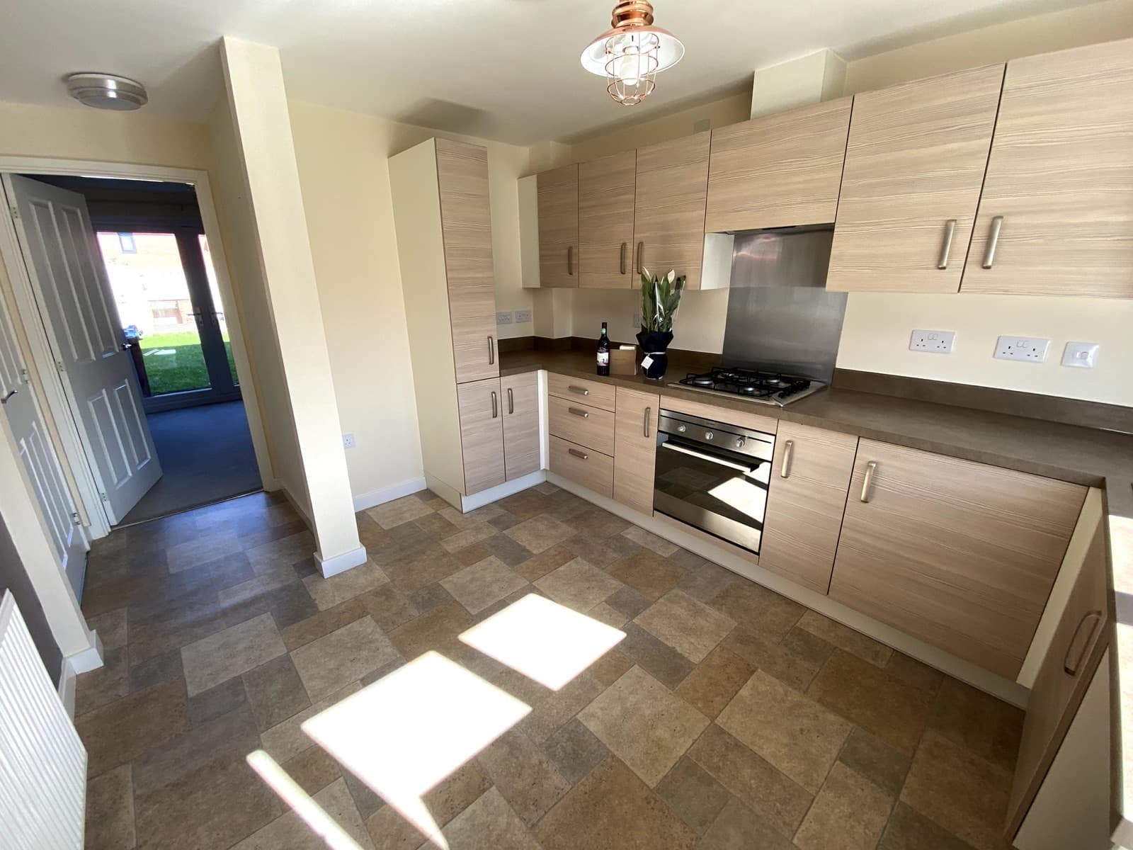 A light oak-effect kitchen with a gas hob, lit by afternoon sun