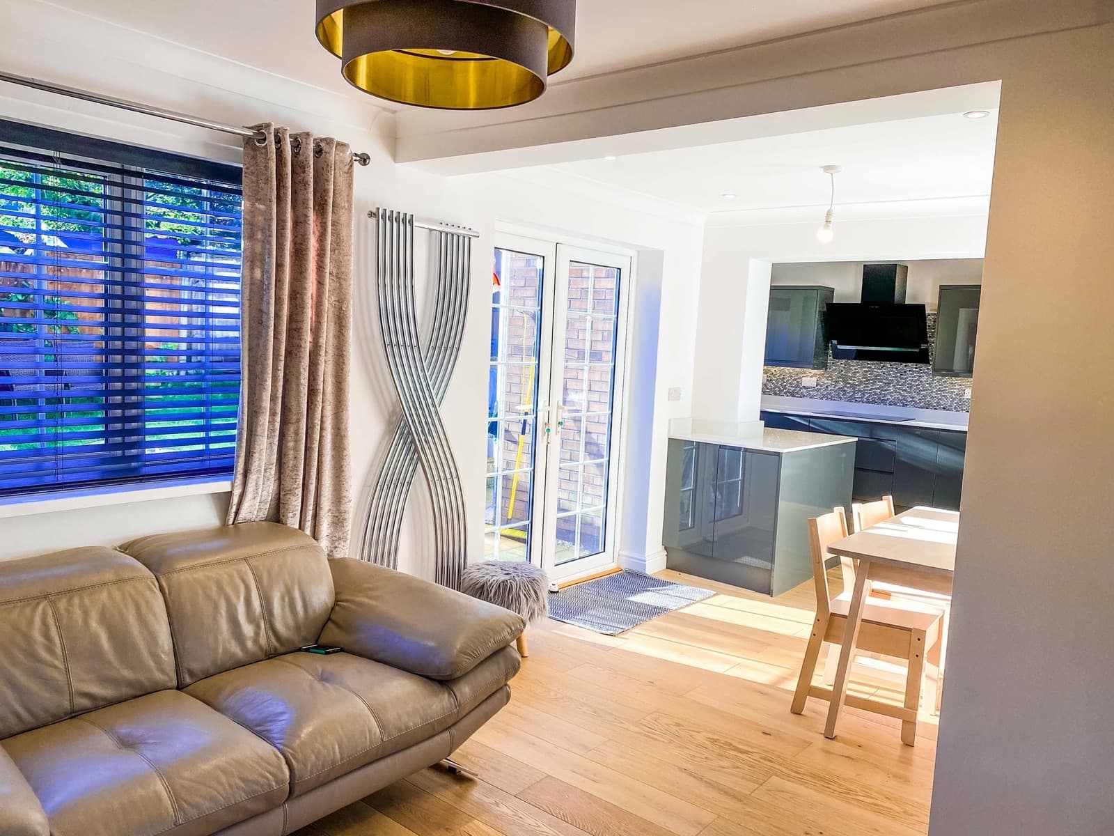 A bright living room with a leather sofa, opening onto a grey kitchen and dining table